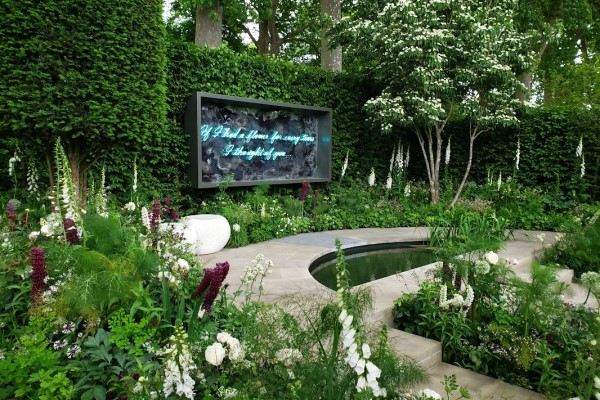 Foto de jardim premiado pelo público do RHS Chelsea Flower Show com flores, árvores e placa de neon